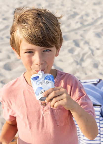 Boy sipping blueberry applesauce pouch from white leaf provisions clean baby food packs